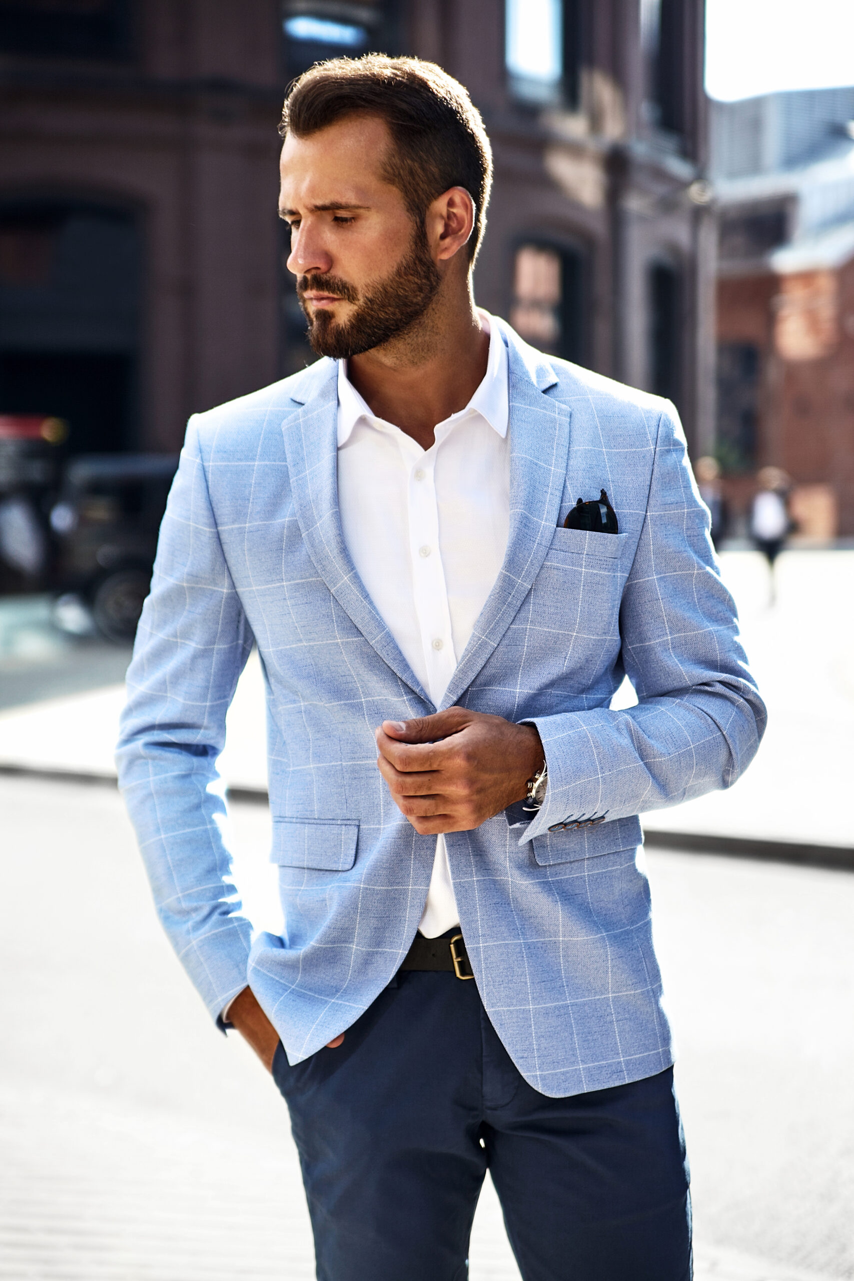 Portrait of sexy handsome fashion businessman model dressed in elegant blue suit posing on street background. Metrosexual